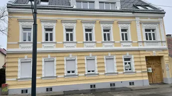 Historisches Gebäude mit gelber Fassade, weißen Fensterläden und modernem Dachausbau.