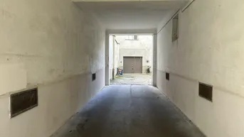 Langer, schmaler Durchgang zu einem Innenhof mit Garagentor am Ende.