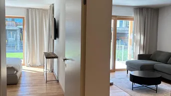 Blick durch einen Türrahmen in ein Schlafzimmer und einen Wohnbereich mit Holzboden und Zugang zum Garten.