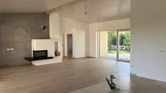 Geräumiges Wohnzimmer mit modernem Kamin, Holzboden und großen Schiebetüren zum Garten.