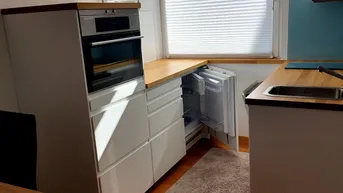 Moderne Einbauküche mit weißen Fronten, Holz-Arbeitsplatten und integrierten Geräten.