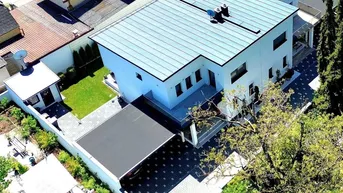 Luftaufnahme eines modernen Einfamilienhauses mit Flachdach, Carport und gepflegtem Gartenbereich.