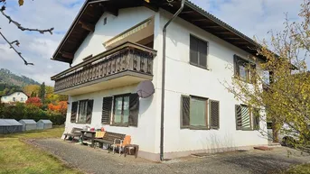 Weißes Einfamilienhaus mit Holzbalkon, Fensterläden und kleinem Sitzbereich im Freien.
