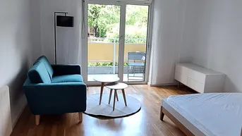 Helles Wohnzimmer mit Holzboden, einem blauen Sofa und Zugang zum Balkon.