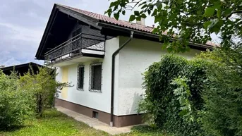 Seitenansicht des Hauses mit Balkon im Obergeschoss und umgebendem Grünbereich.