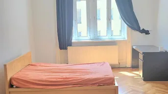 Helles Schlafzimmer mit Fischgrätparkett, einem Bett und einem Schreibtisch am Fenster.