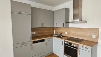 Moderne Einbauküche in Grau mit Holzakzenten, ausgestattet mit Herd und Dunstabzugshaube.
