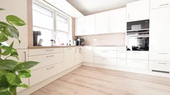 Helle, moderne Küche mit weißen Hochglanzfronten, integrierten Geräten und großem Fenster.