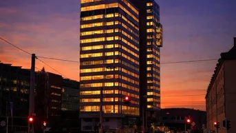 Hohes Bürogebäude bei Sonnenuntergang mit beleuchteten Fenstern und Straßenansicht in der Stadt.