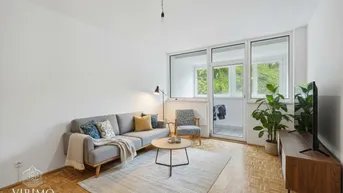 Helles Wohnzimmer mit Parkettboden, modernem Sofa und Zugang zum Balkon mit Grünblick.