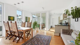 Heller offener Wohn- und Essbereich mit Holzboden, integrierter Küche und Zugang zum Balkon.