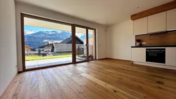 Helles Wohnzimmer mit offener Küche, Holzboden und Bergblick durch große Fenster.