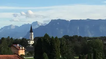 Blick auf eine Kirche und eine Bergkette unter blauem Himmel.
