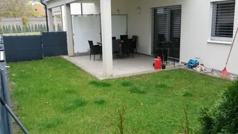 Gepflegter Gartenbereich mit überdachter Terrasse und Balkon im Obergeschoss.
