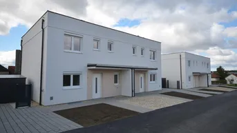 Moderne Reihenhäuser in Neubaugebiet mit gepflasterten Zufahrten und Rollläden an den Fenstern.