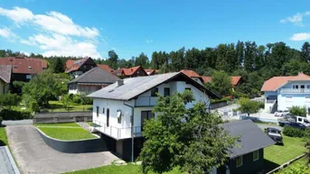 Ländliches Einfamilienhaus mit Garten und umliegender Natur unter blauem Himmel.