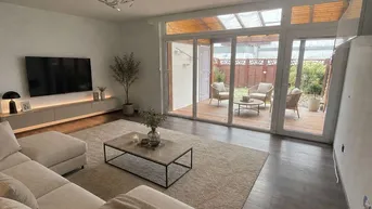 Modernes Wohnzimmer mit beigem Sofa, dunklem Holzboden und Zugang zu einer überdachten Terrasse.