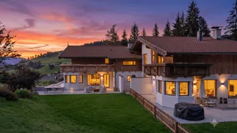 Großzügige alpine Villa bei Sonnenuntergang mit mehreren Terrassen und weitläufigem Gartenbereich.