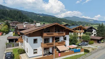 Gebäude in alpiner Umgebung mit Balkonen, Terrasse und Bergblick unter blauem Himmel.