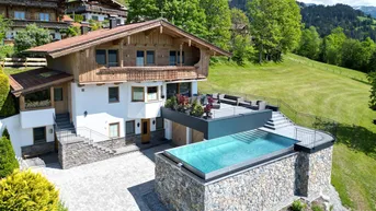 Großzügiges Chalet mit Infinity-Pool, großer Terrasse und Bergblick in grüner Umgebung.