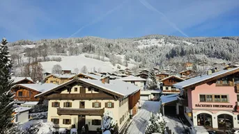 Panoramablick auf ein verschneites Dorf mit traditionellen Häusern und majestätischen Bergen im Hintergrund unter blauem Himmel.