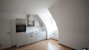 Moderne Küchenzeile in einem Dachgeschossraum mit Schrägdecke, Holzboden und integrierten Geräten.