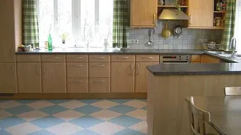 Helle Küche mit Holzschränken, kariertem Boden und Blick nach draußen.