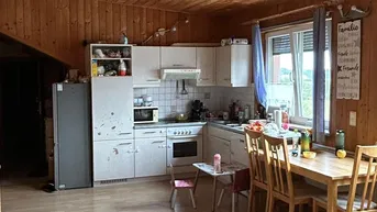 Helle Wohnküche mit Holzwänden und -decke, hellem Laminatboden und Essbereich am Fenster.