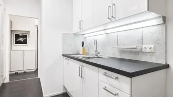 Kleine, moderne Küche mit weißen Hochglanzschränken, dunkler Arbeitsplatte und Spülbecken.