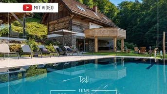 Rustikales Holzhaus mit großem Außenpool und umgebender Naturlandschaft, inklusive Video-Hinweis.