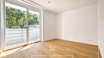 Helles, leeres Zimmer mit Holzboden und Zugang zu einem Balkon.