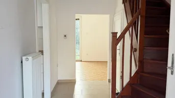 Heller Flur mit Fliesenboden, Heizkörper und Holztreppe, die in die obere Etage führt.