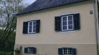 Historisches Gebäude mit beiger Fassade, blauen Fensterläden und einem gepflegten Rasen.