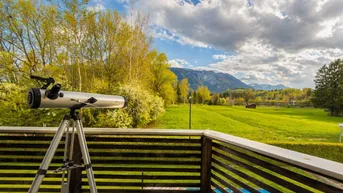 Balkon mit Teleskop und weitem Blick über grüne Felder und Berge in der Ferne.