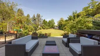 Große gepflasterte Terrasse mit bequemen Loungemöbeln und weitem Blick in den grünen Garten.