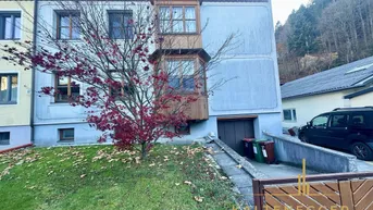 Fassade eines Mehrfamilienhauses mit Holzbalkonen und einem kleinen Vorgarten.