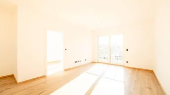 Helles, leeres Zimmer mit Holzboden und Zugang zu einem französischen Balkon, durchflutet von Sonnenlicht.