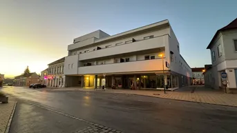 Modernes Gebäude mit klaren Linien und großen Fenstern in städtischer Umgebung bei Dämmerung.