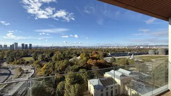 Weitläufiger Ausblick von einem Balkon über grüne Parkanlagen und die Stadt Wien.