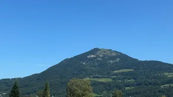 Panoramablick auf die umliegende Berglandschaft und die Dächer der Häuser unter blauem Himmel.