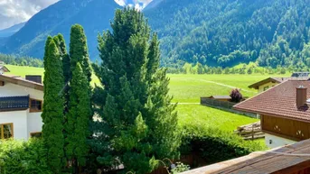 Blick von einem Balkon auf eine malerische Berglandschaft mit grünen Wiesen und Wäldern.