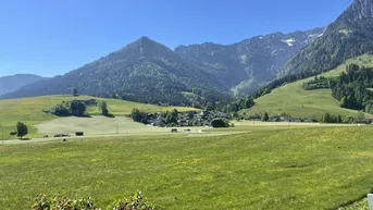 Grüne Wiesen und majestätische Berge umrahmen ein idyllisches Dorf unter strahlend blauem Himmel.