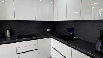 Moderne Küche mit weißen Hochglanzschränken, schwarzen Arbeitsplatten und Induktionskochfeld.
