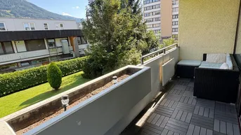 Geräumiger Balkon mit modernen Bodenfliesen und gemütlicher Sitzecke, umgeben von Grünflächen.