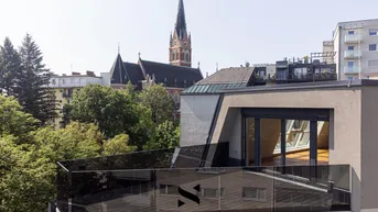 Moderne Dachterrasse mit Glasgeländer und Blick auf die Stadt und eine Kirche.