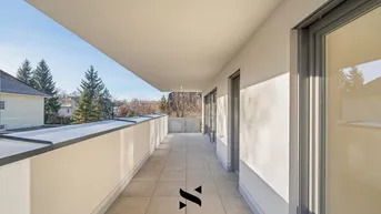 Langer, sonniger Balkon mit Fliesenboden und Blick auf Bäume und Häuser.