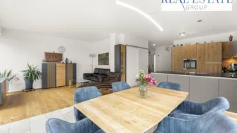 Heller offener Wohn-Essbereich mit moderner Küche, Holzboden und blauen Esszimmerstühlen.