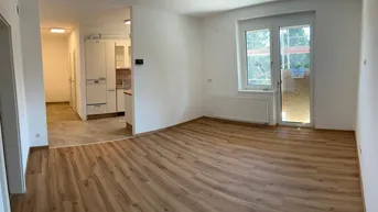Helles Wohnzimmer mit neuem Laminatboden und Zugang zu einem Balkon, offen zur Küche.