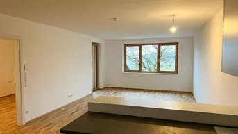 Heller, offener Wohnbereich mit Parkettboden und Blick ins Grüne durch das Fenster.