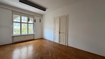 Helles Zimmer mit Fischgrätparkettboden, hohen Decken und großen Fenstern.